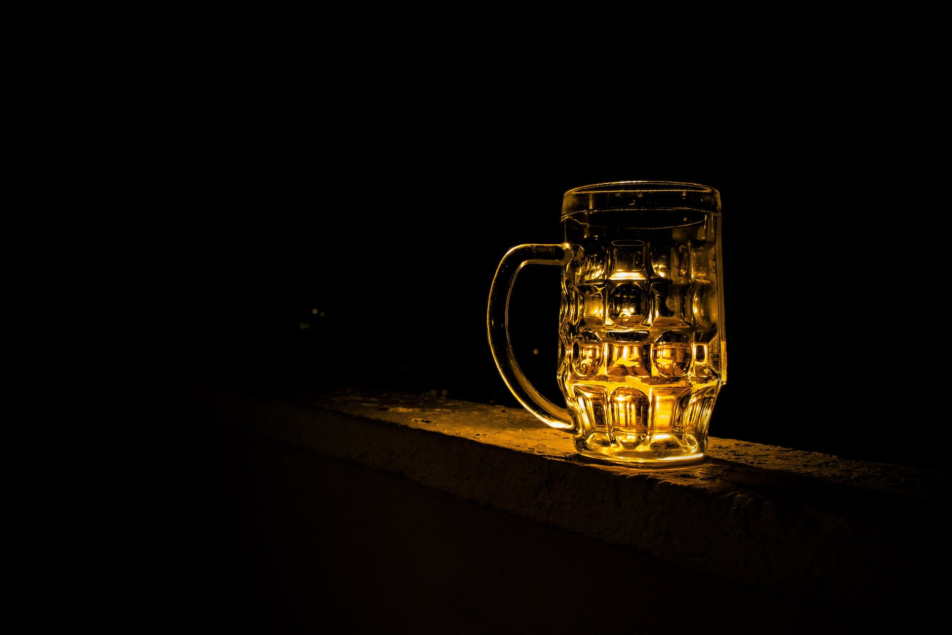 A glass mug filled with beer with a black background. 