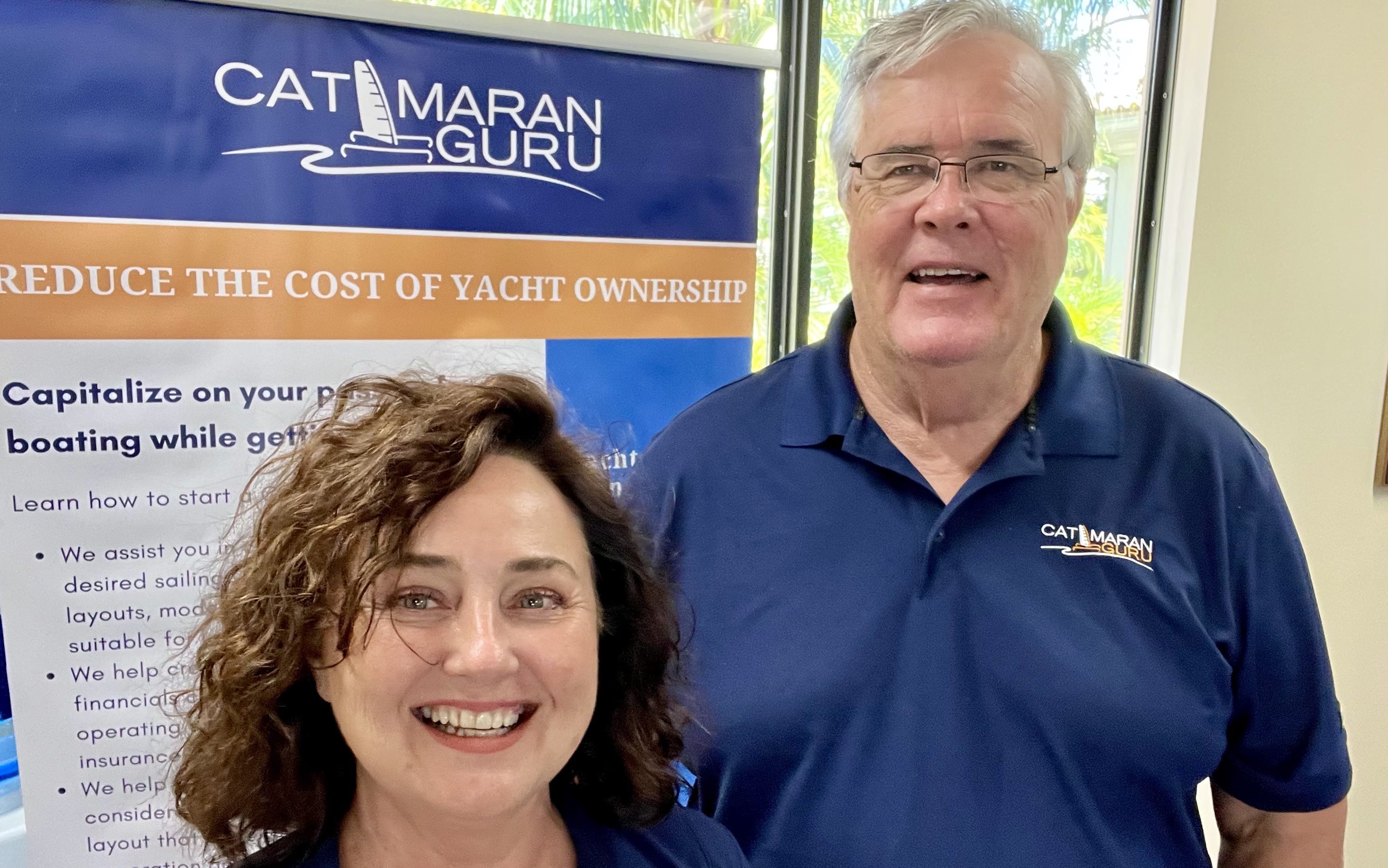 Estelle and Stephen selfie wearing blue Catamaran with a Catamaran banner as their background.