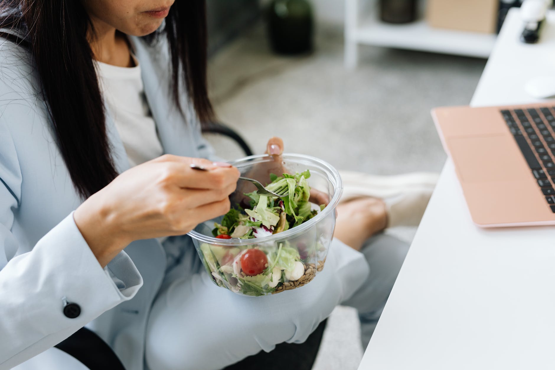 A woman eating a salad at her desk. 