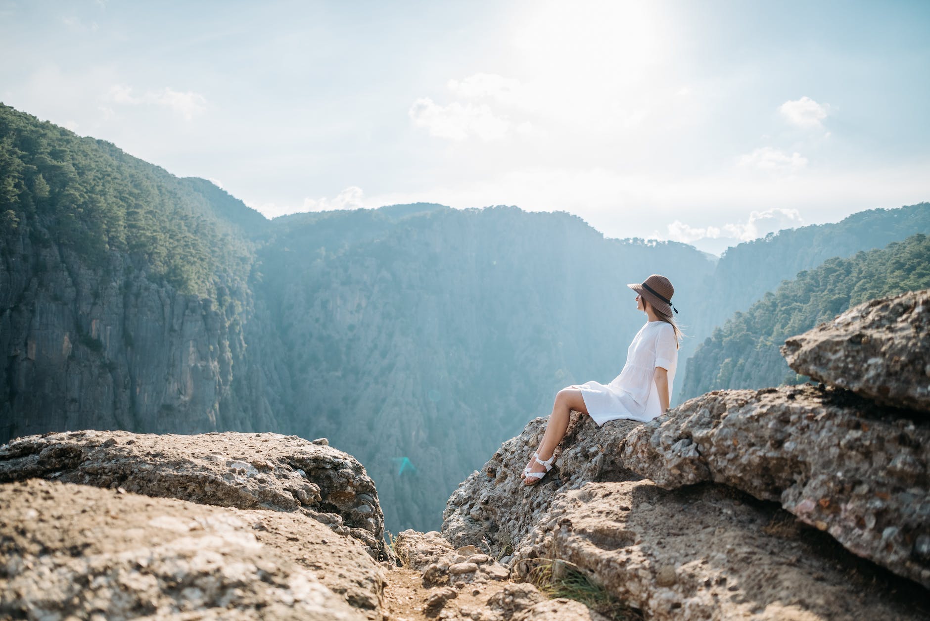 A woman wearing a white dress at the top a mountain sitting in a rock. 