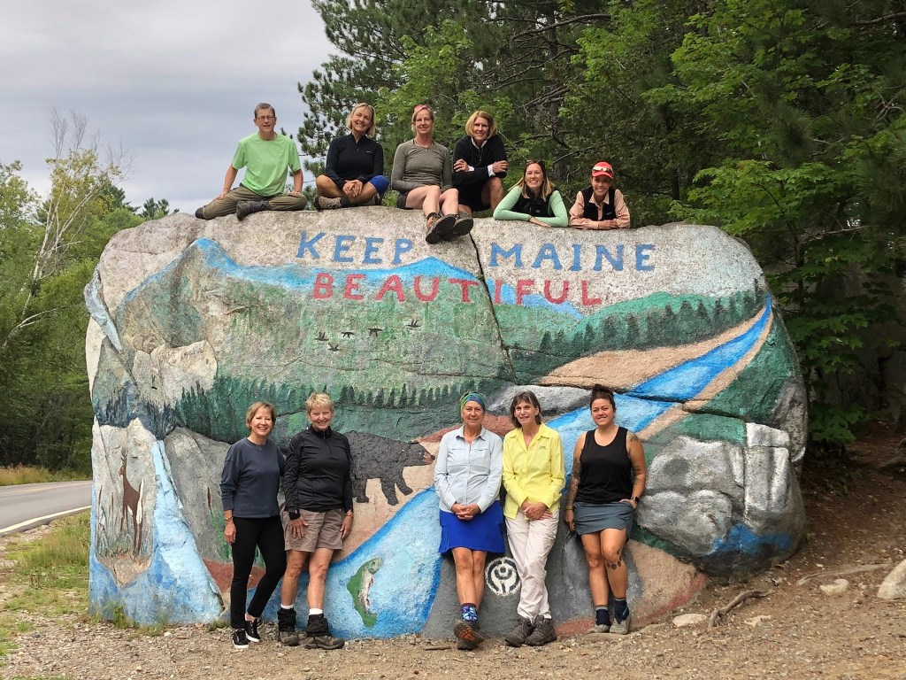 A group of explores in front of a big rock painted with a sign that says
"Keep Maine Beautiful".