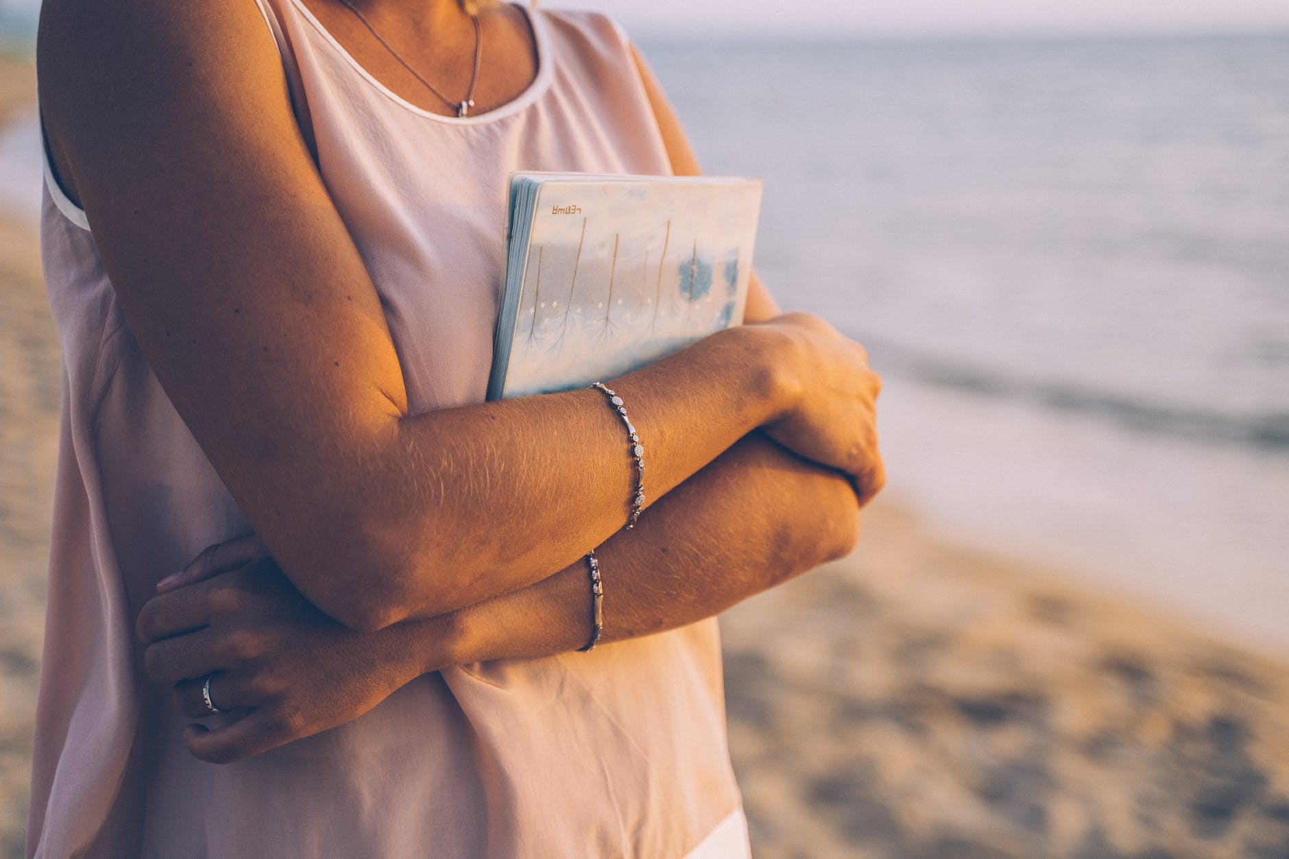 A women standing in front of the sea hugging a book. 